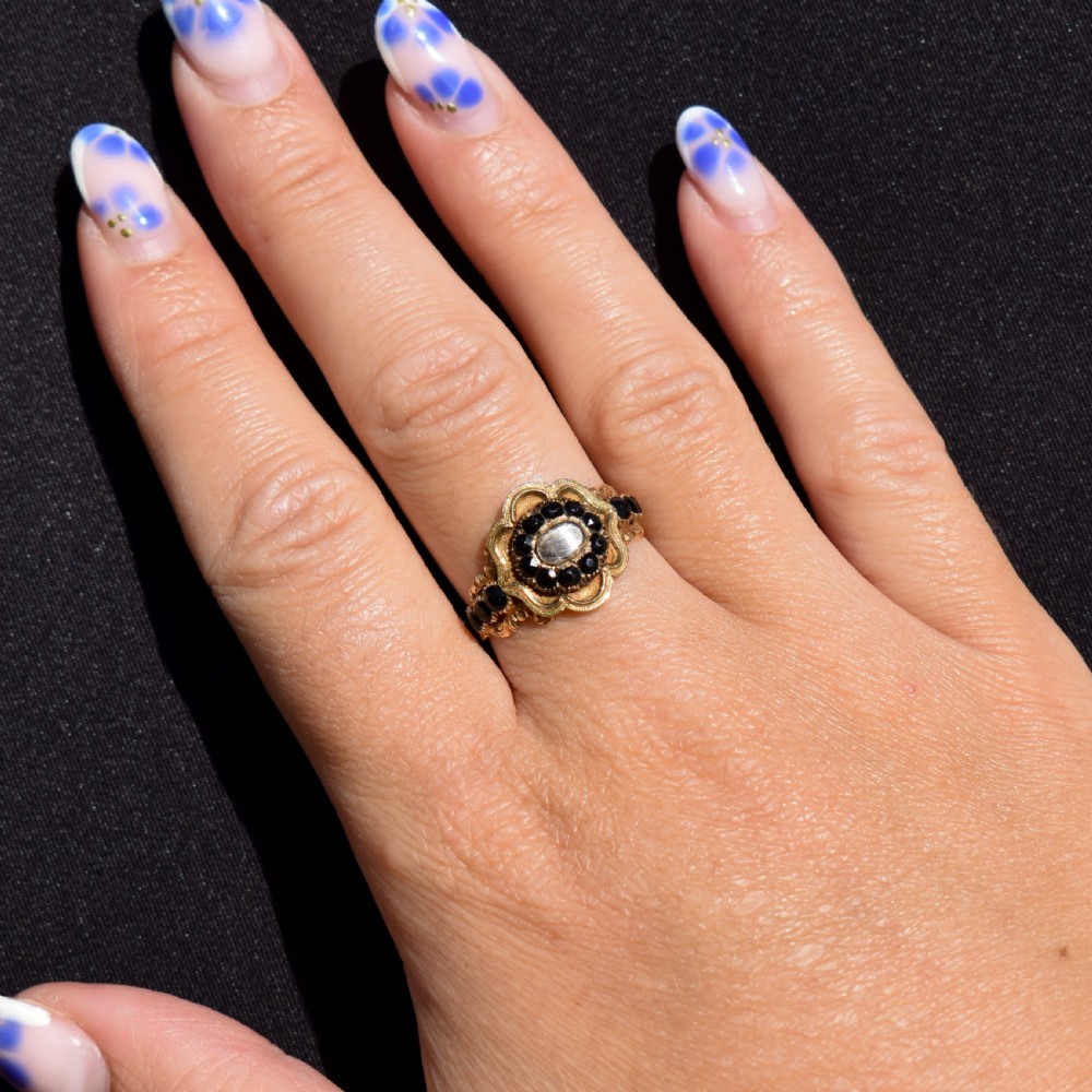 A Georgian gold ring featuring a central woven hair panel set under glass, surrounded by a cluster of faceted black jet stones. View X