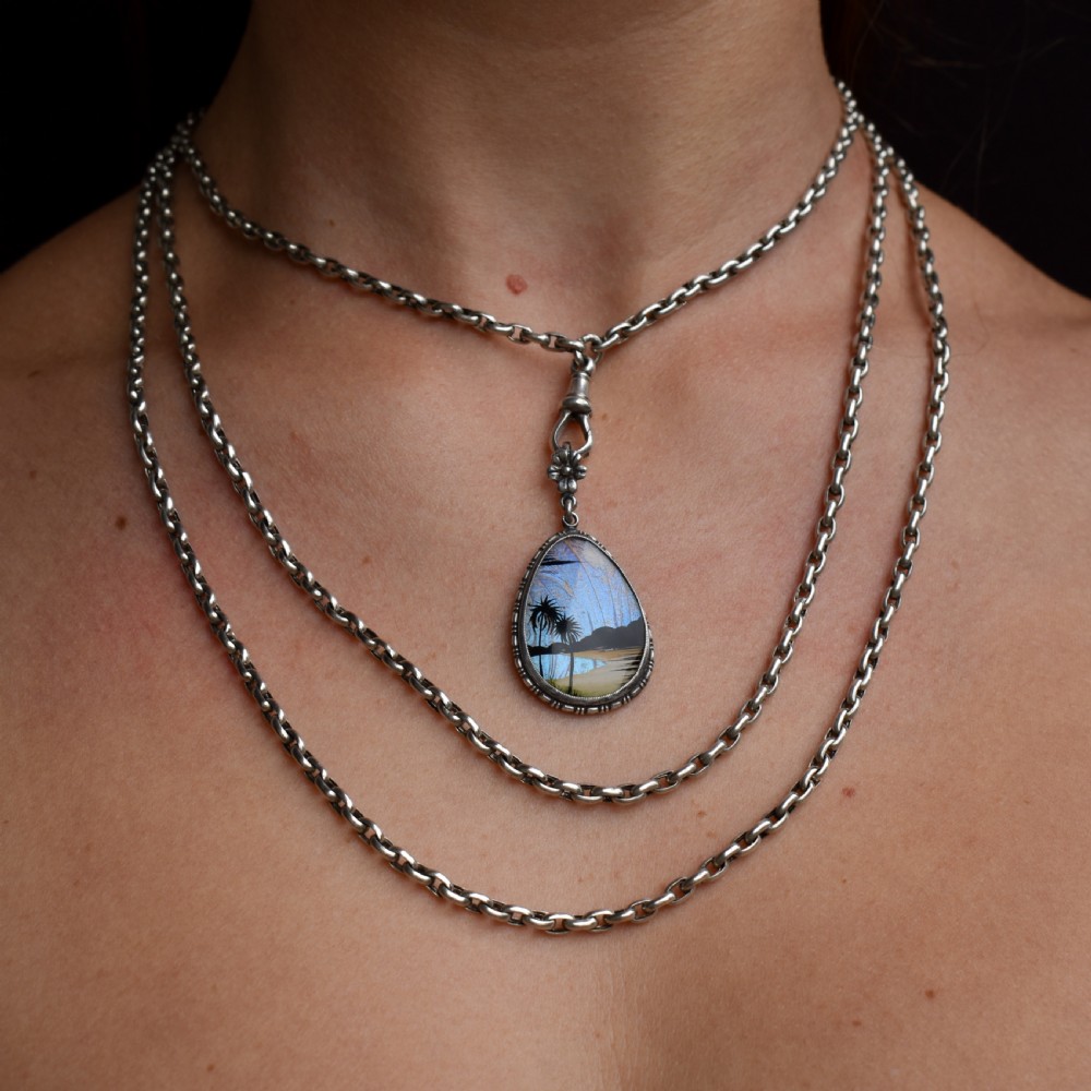 An Art Deco teardrop-shaped sterling silver pendant featuring a reverse-painted tropical palm scene over an iridescent blue butterfly wing. View II