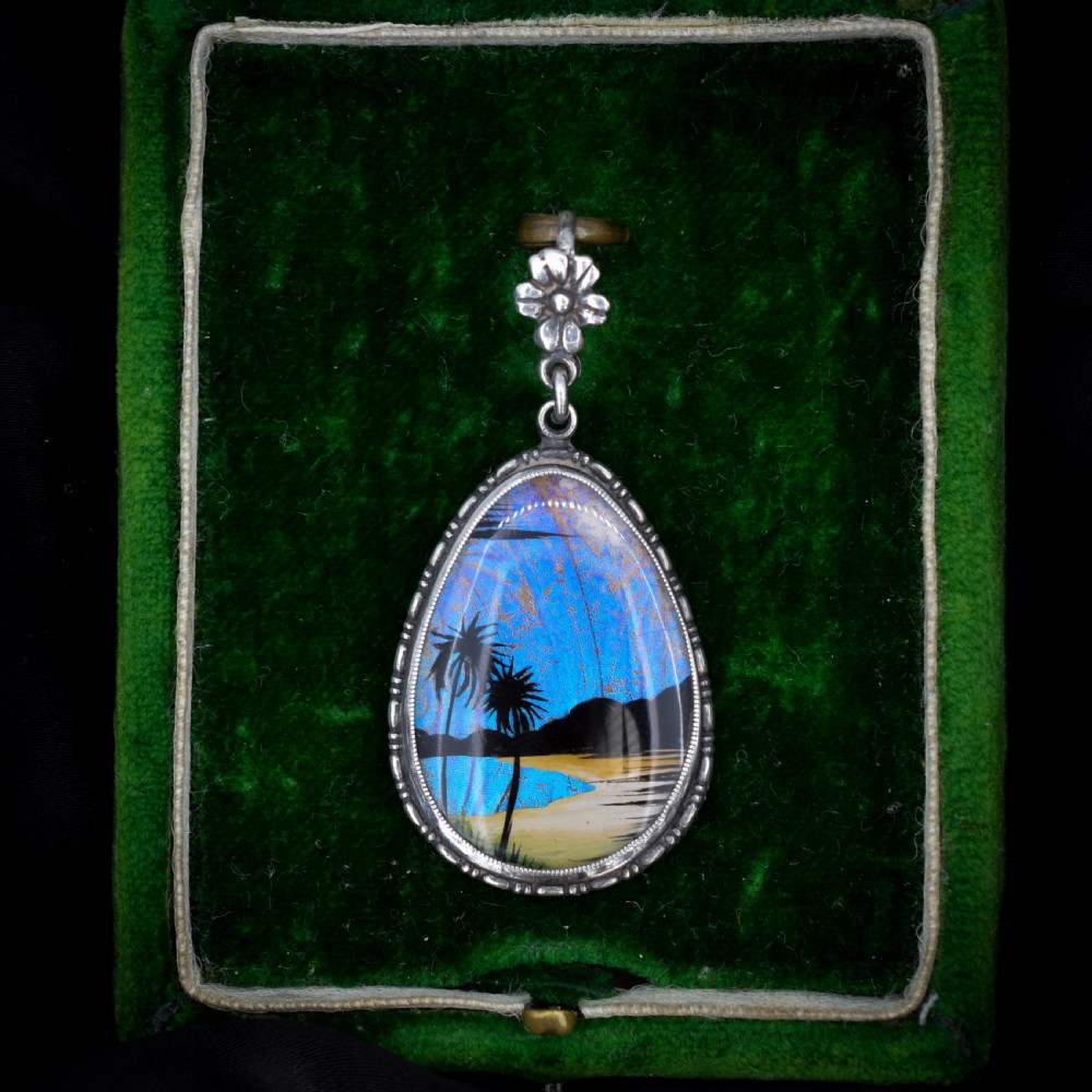 An Art Deco teardrop-shaped sterling silver pendant featuring a reverse-painted tropical palm scene over an iridescent blue butterfly wing. View III