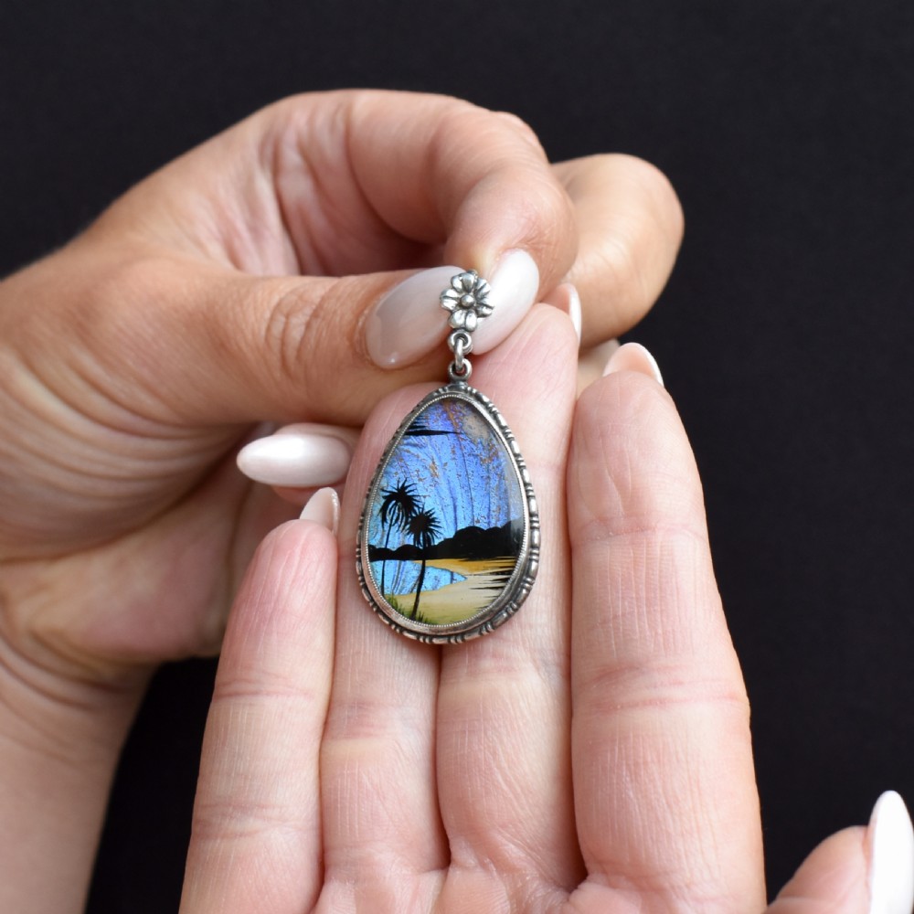 An Art Deco teardrop-shaped sterling silver pendant featuring a reverse-painted tropical palm scene over an iridescent blue butterfly wing. View IV