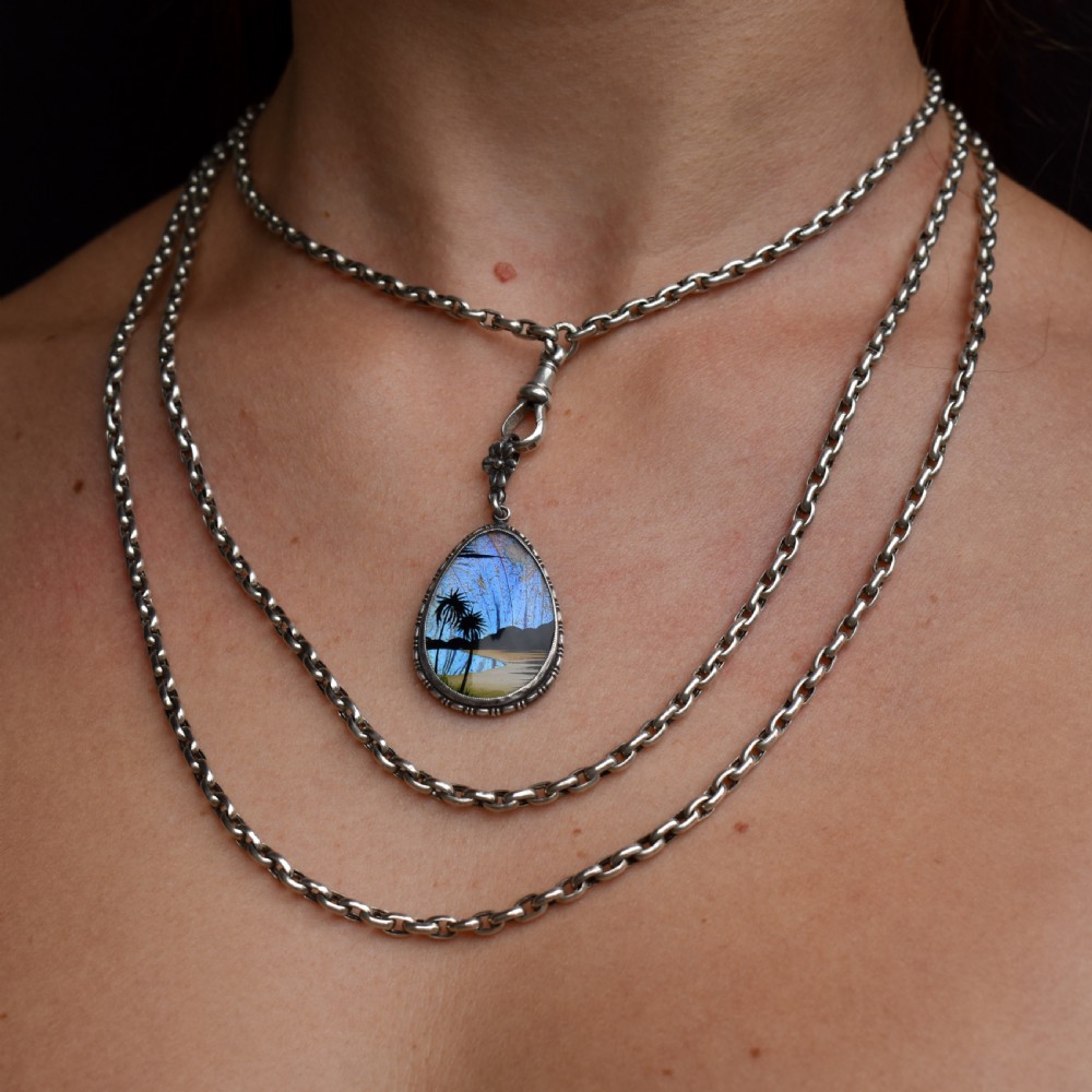 An Art Deco teardrop-shaped sterling silver pendant featuring a reverse-painted tropical palm scene over an iridescent blue butterfly wing. View VI