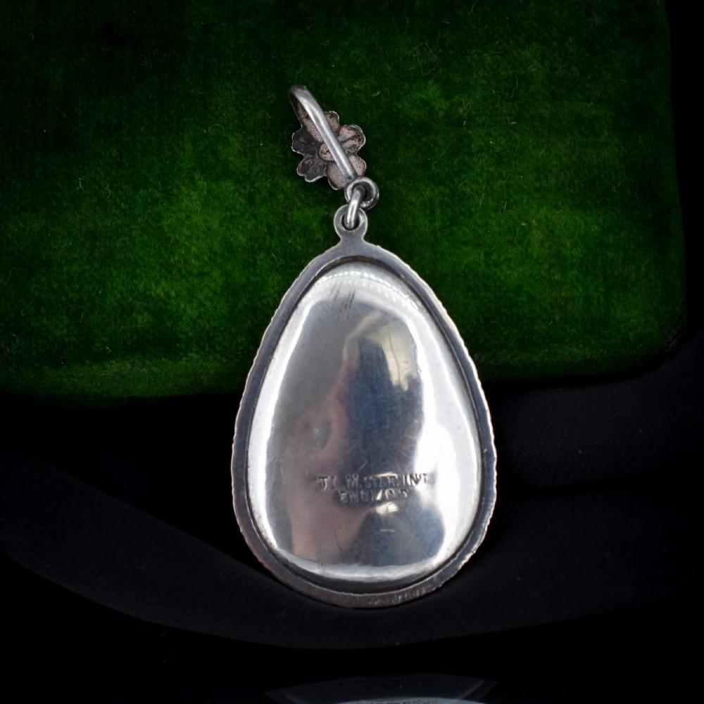 An Art Deco teardrop-shaped sterling silver pendant featuring a reverse-painted tropical palm scene over an iridescent blue butterfly wing. View VII