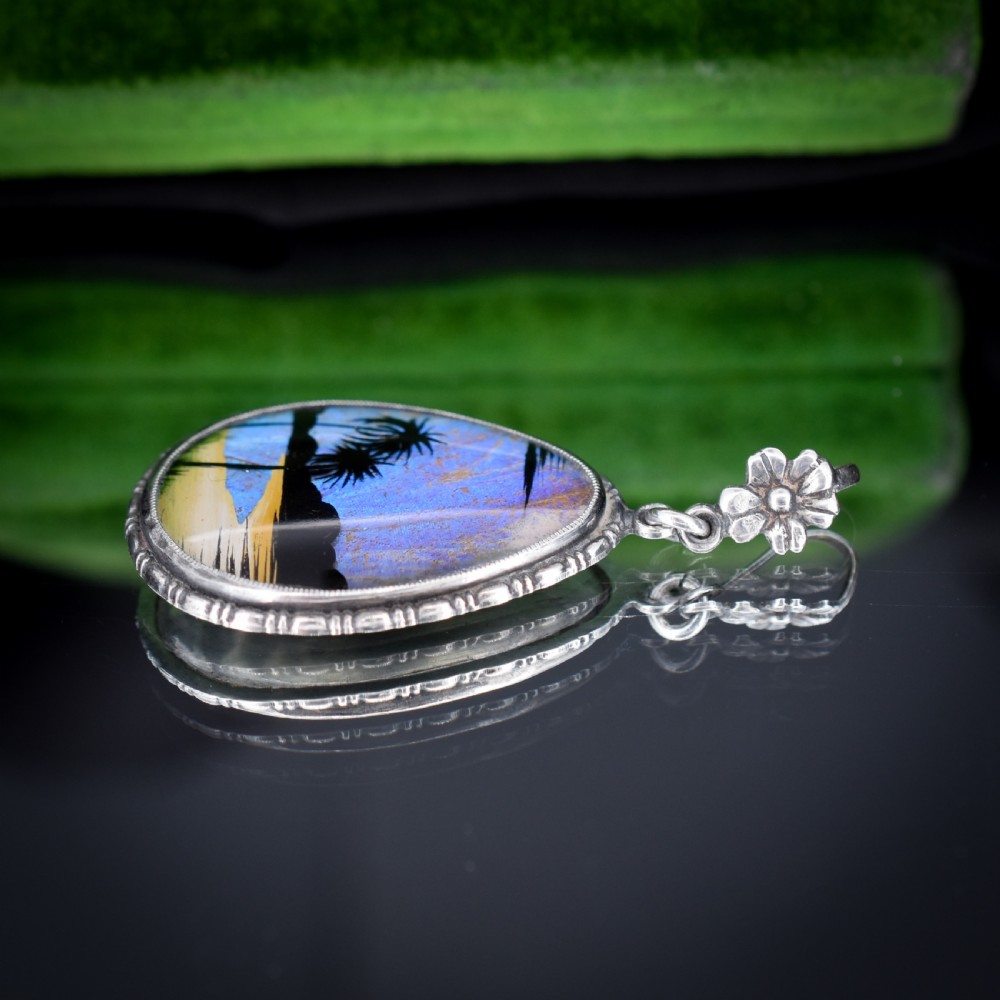 An Art Deco teardrop-shaped sterling silver pendant featuring a reverse-painted tropical palm scene over an iridescent blue butterfly wing. View VIII