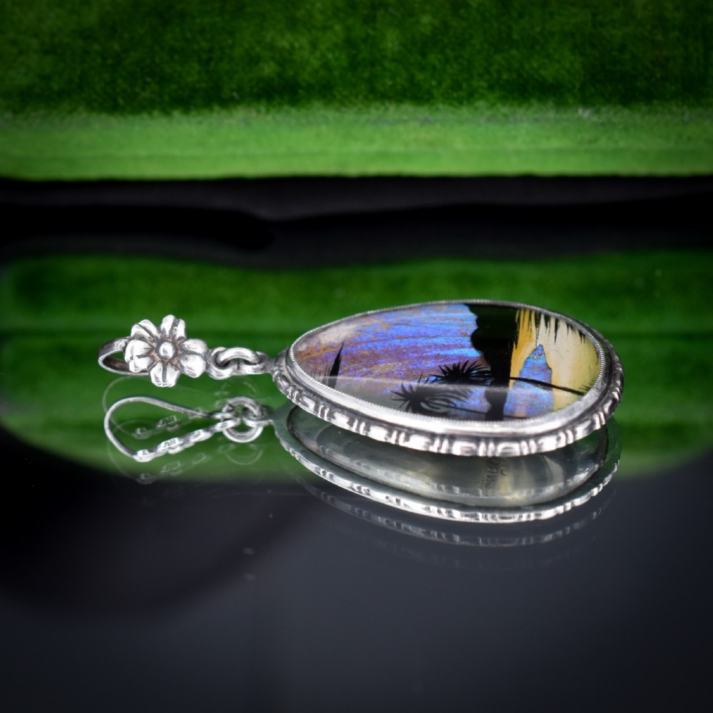 An Art Deco teardrop-shaped sterling silver pendant featuring a reverse-painted tropical palm scene over an iridescent blue butterfly wing. View IX
