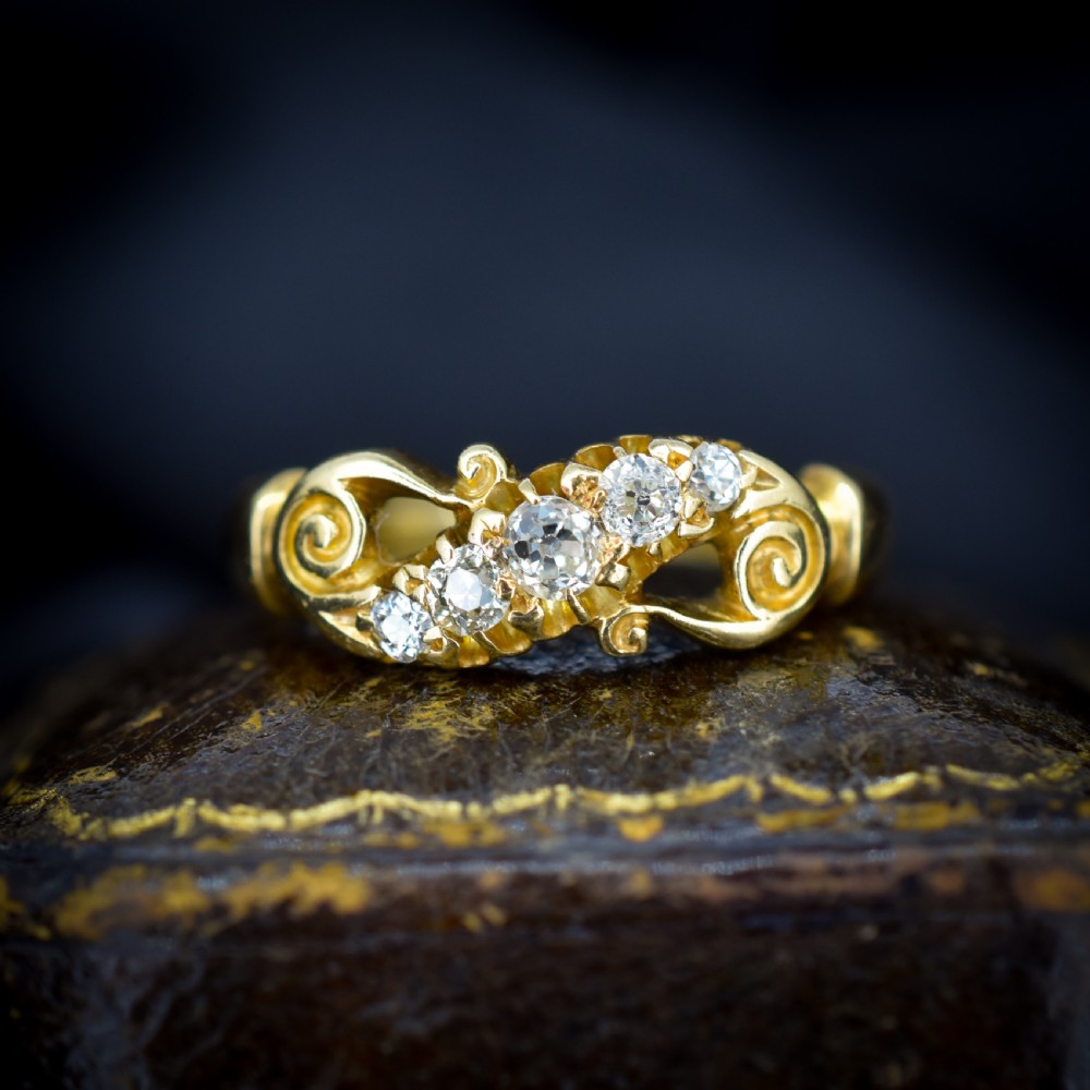 An 18ct yellow gold ring set with five graduated old-cut diamonds across a carved scrollwork band.