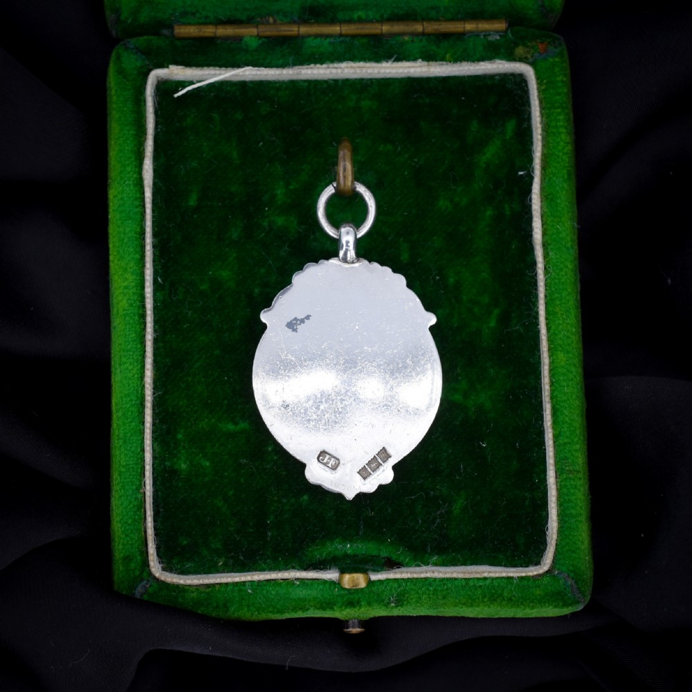 A circular silver Art Deco football medal pendant featuring an embossed figure of a footballer with a ball, framed by scrollwork edges and a top suspension ring. View IV