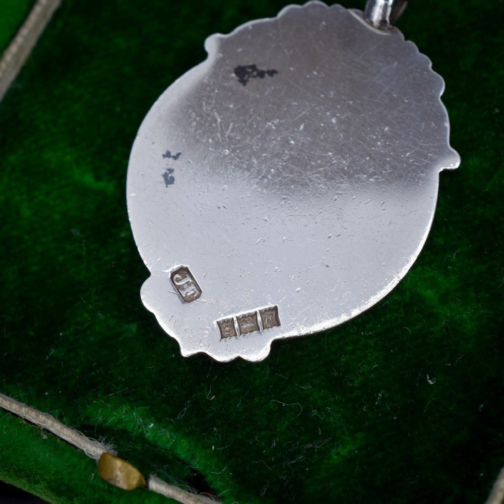 A circular silver Art Deco football medal pendant featuring an embossed figure of a footballer with a ball, framed by scrollwork edges and a top suspension ring. View VI