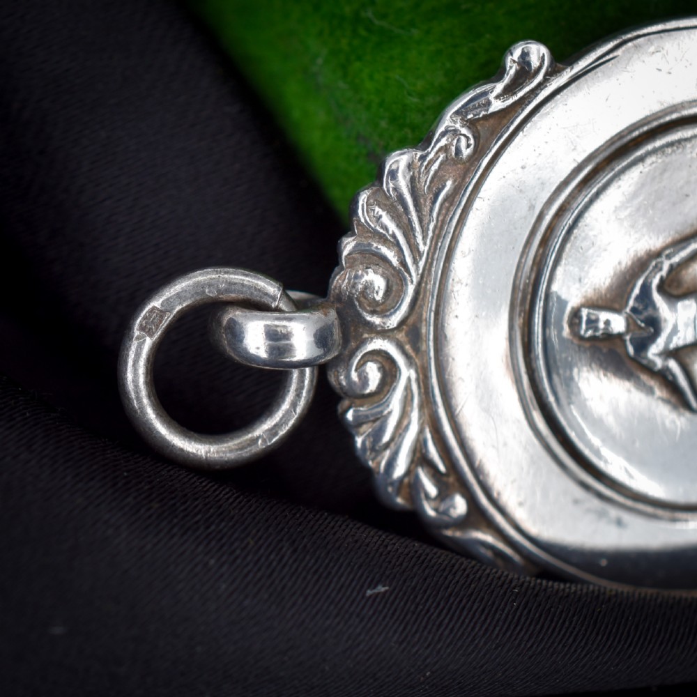 A circular silver Art Deco football medal pendant featuring an embossed figure of a footballer with a ball, framed by scrollwork edges and a top suspension ring. View VII