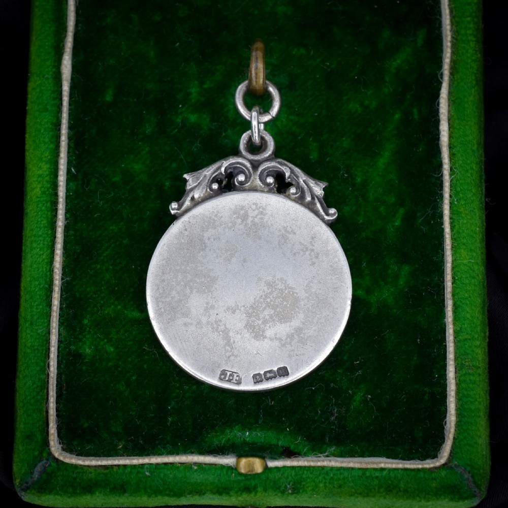 A circular silver Art Deco medallion depicting a raised relief figure of a cricketer with a bat beside wickets, finished with a scroll suspension loop. View VI