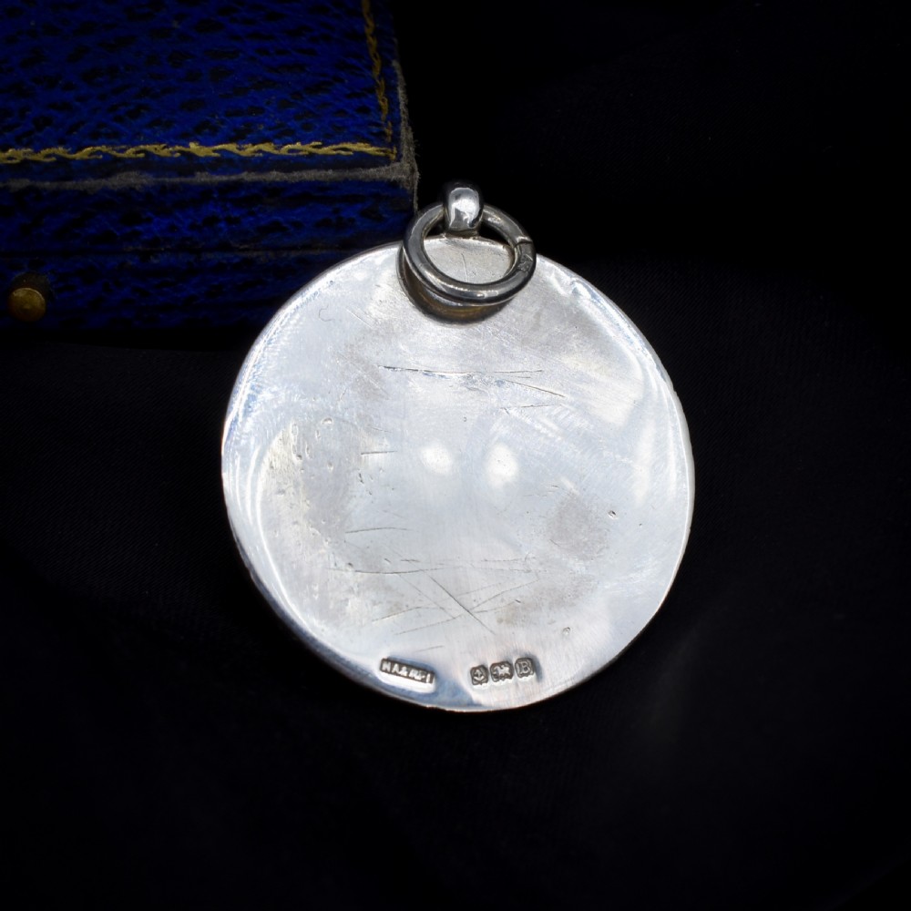 A circular silver Art Deco medallion depicting two football players in relief with a football, suspended from a top loop. View IV