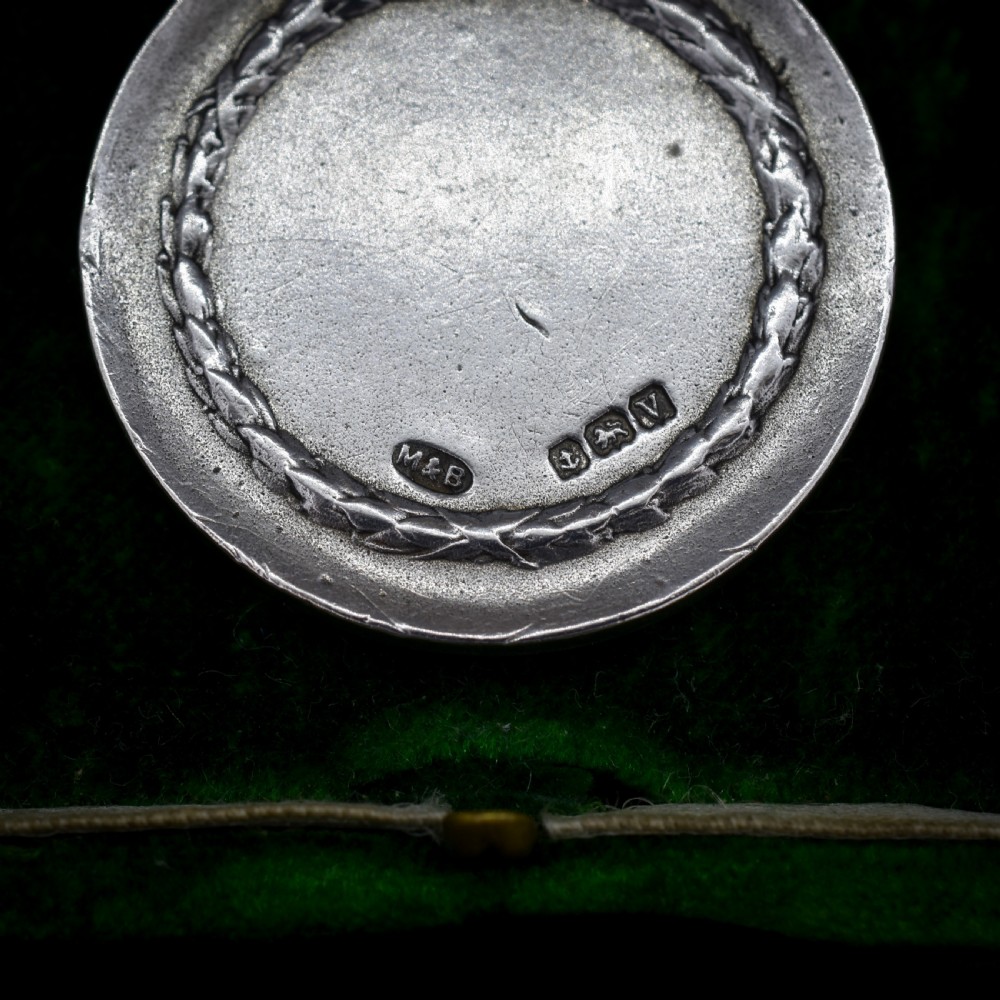 A circular silver medallion featuring a golfer rendered in relief mid-swing with a suspension ring attached to the top. View II