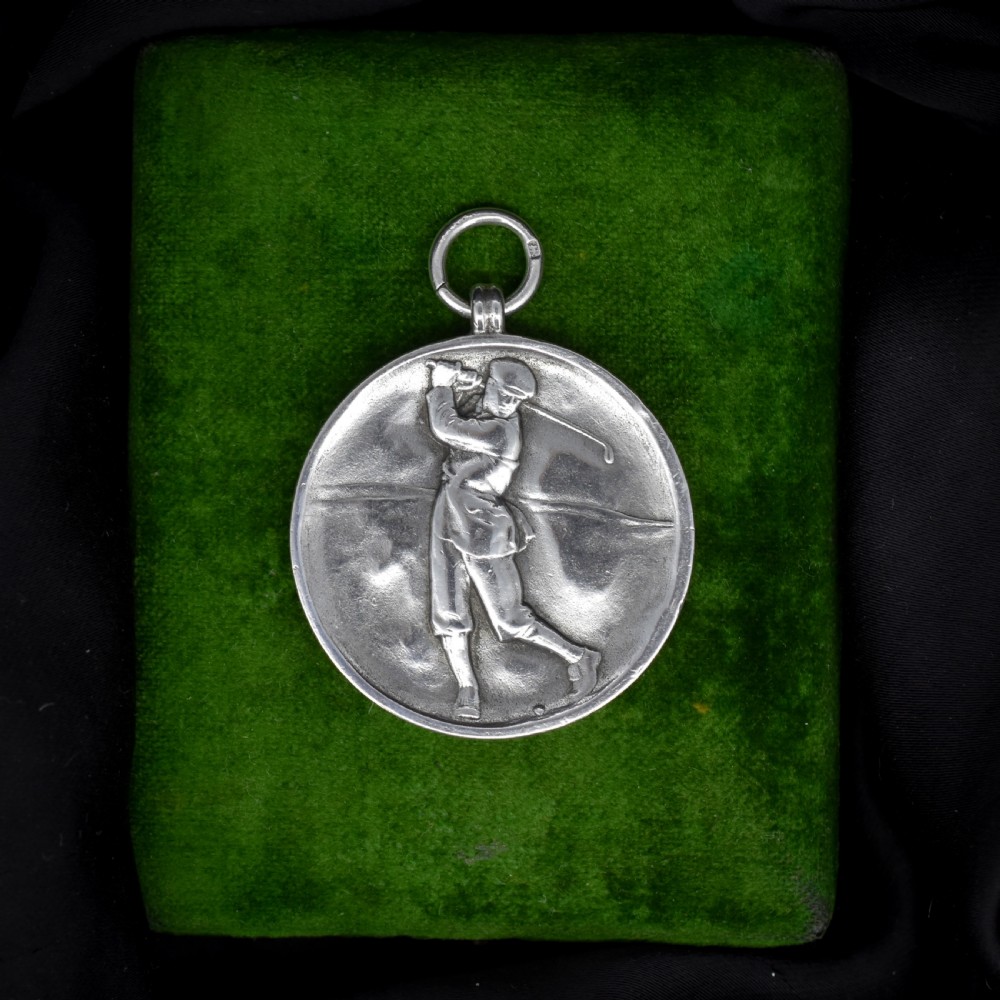 A circular silver medallion featuring a golfer rendered in relief mid-swing with a suspension ring attached to the top. View V