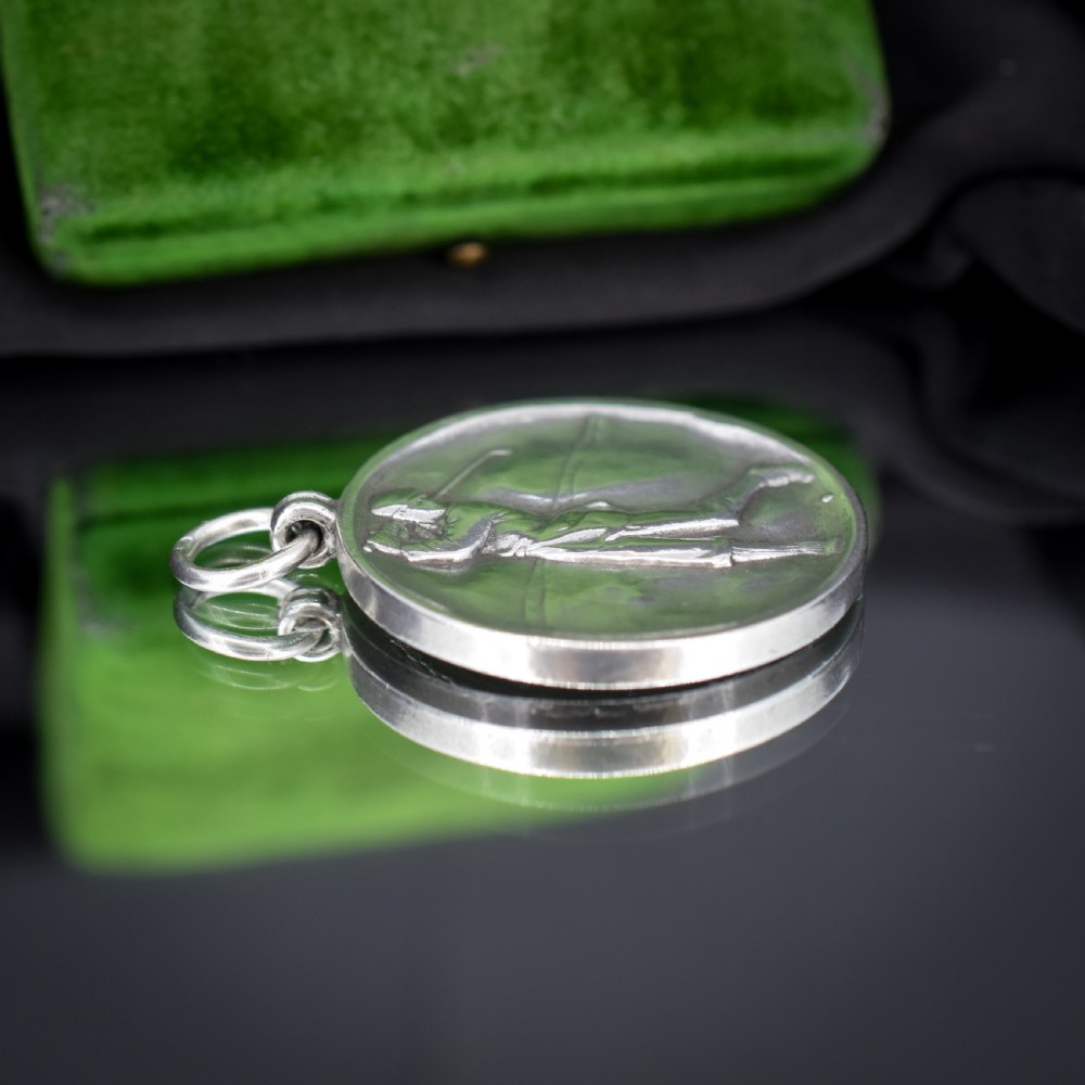 A circular silver medallion featuring a golfer rendered in relief mid-swing with a suspension ring attached to the top. View VI