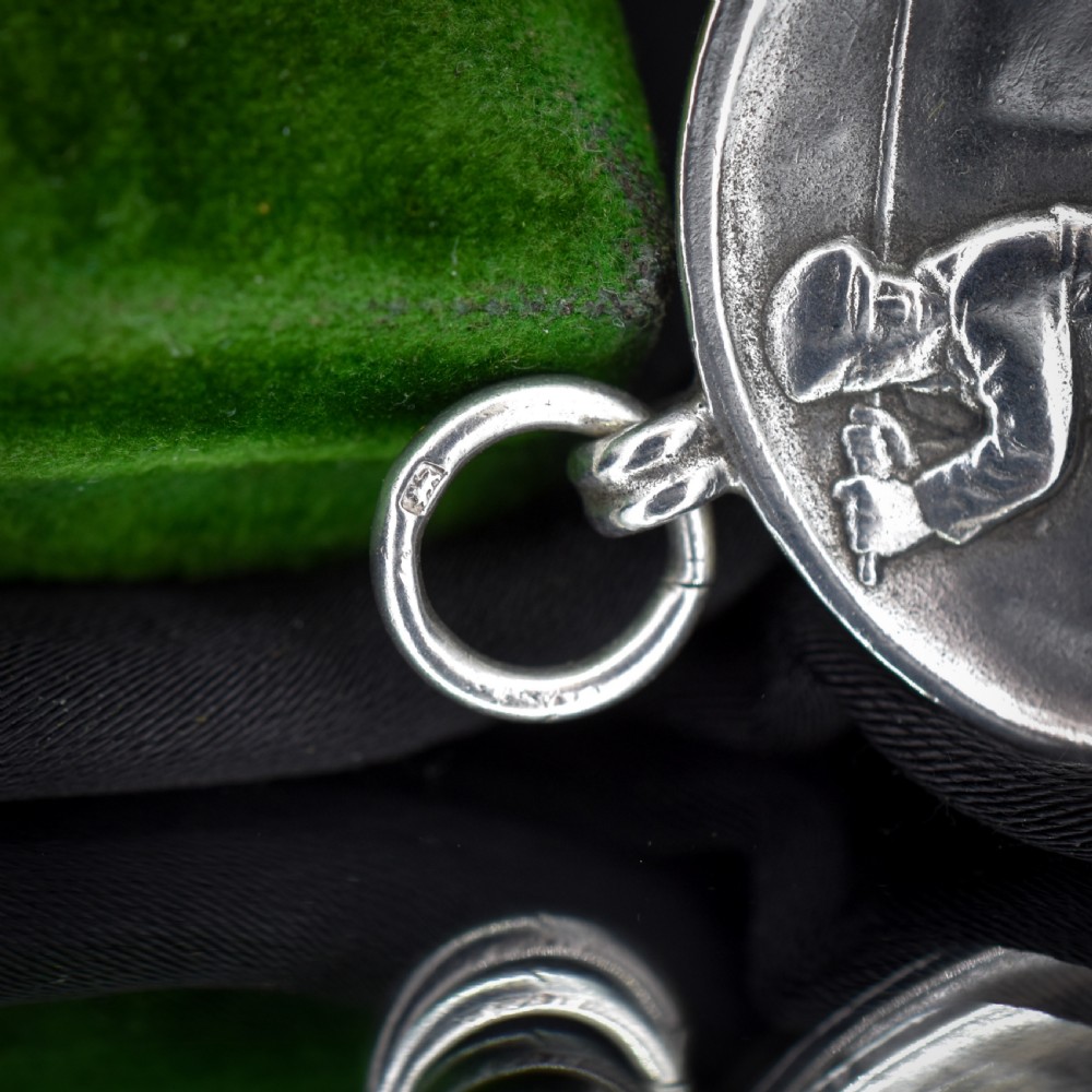 A circular silver medallion featuring a golfer rendered in relief mid-swing with a suspension ring attached to the top. View VII