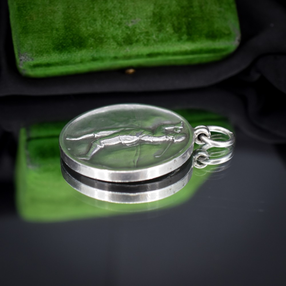A circular silver medallion featuring a golfer rendered in relief mid-swing with a suspension ring attached to the top. View VIII