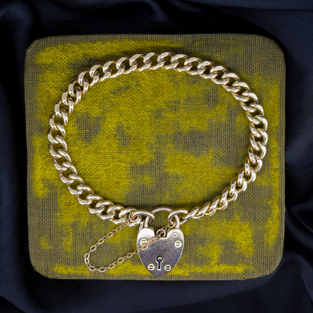 An antique 9ct yellow gold curb link chain bracelet fitted with a heart-shaped padlock clasp and an attached safety chain.