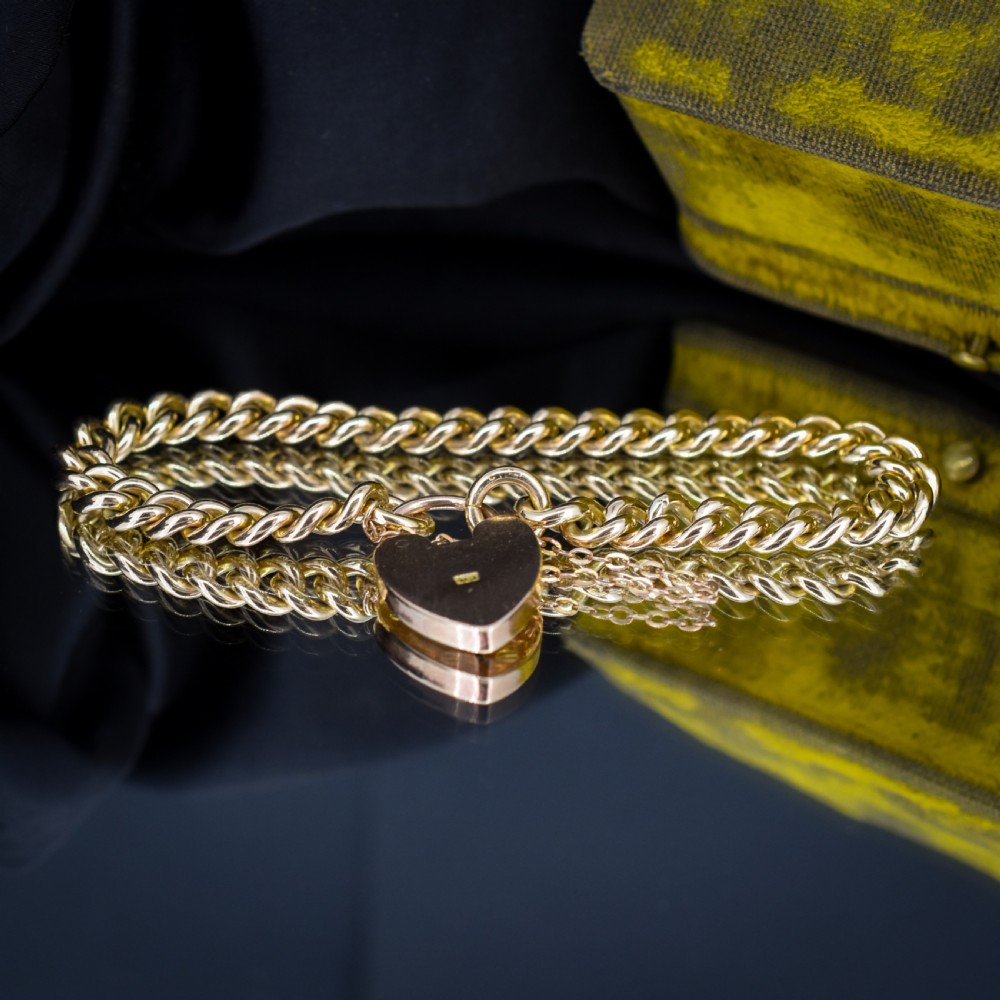 An antique 9ct yellow gold curb link chain bracelet fitted with a heart-shaped padlock clasp and an attached safety chain. View II