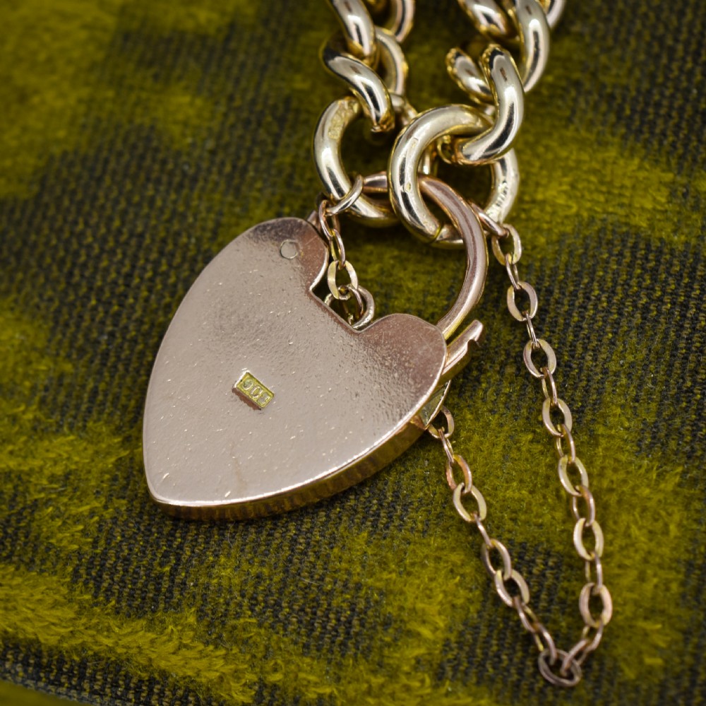An antique 9ct yellow gold curb link chain bracelet fitted with a heart-shaped padlock clasp and an attached safety chain. View V