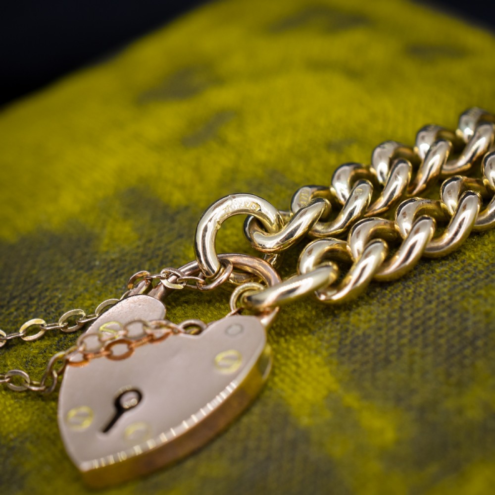 An antique 9ct yellow gold curb link chain bracelet fitted with a heart-shaped padlock clasp and an attached safety chain. View VI