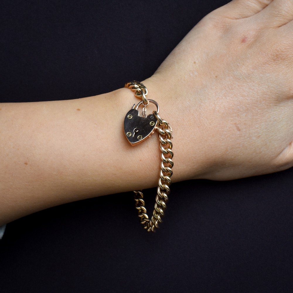 An antique 9ct yellow gold curb link chain bracelet fitted with a heart-shaped padlock clasp and an attached safety chain. View IX