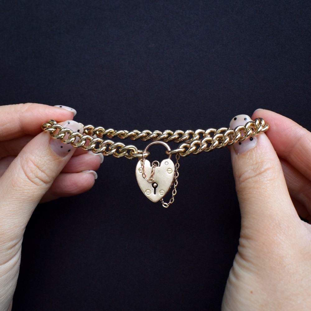 An antique 9ct yellow gold curb link chain bracelet fitted with a heart-shaped padlock clasp and an attached safety chain. View X