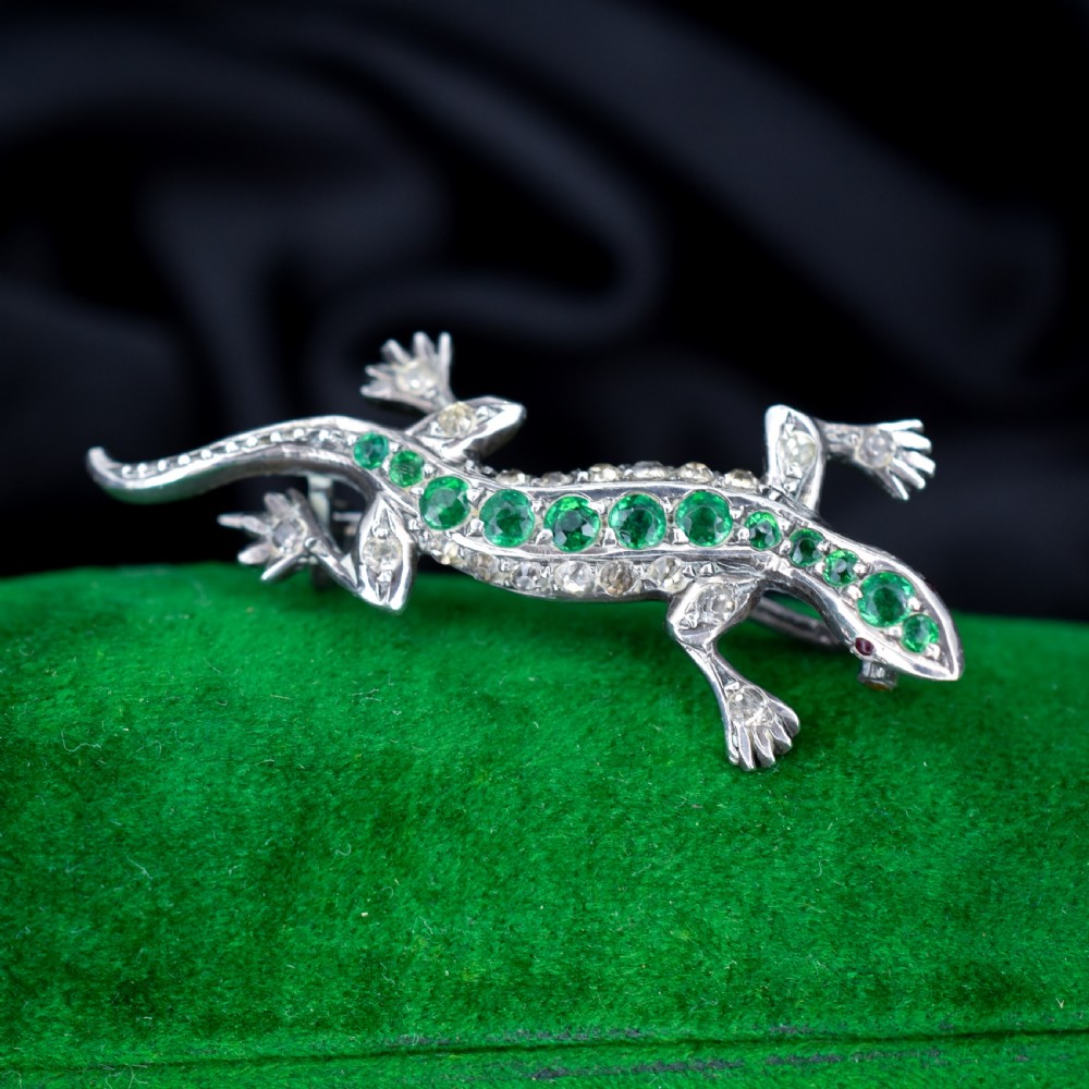 A Victorian silver lizard brooch set with green and clear paste stones. View V