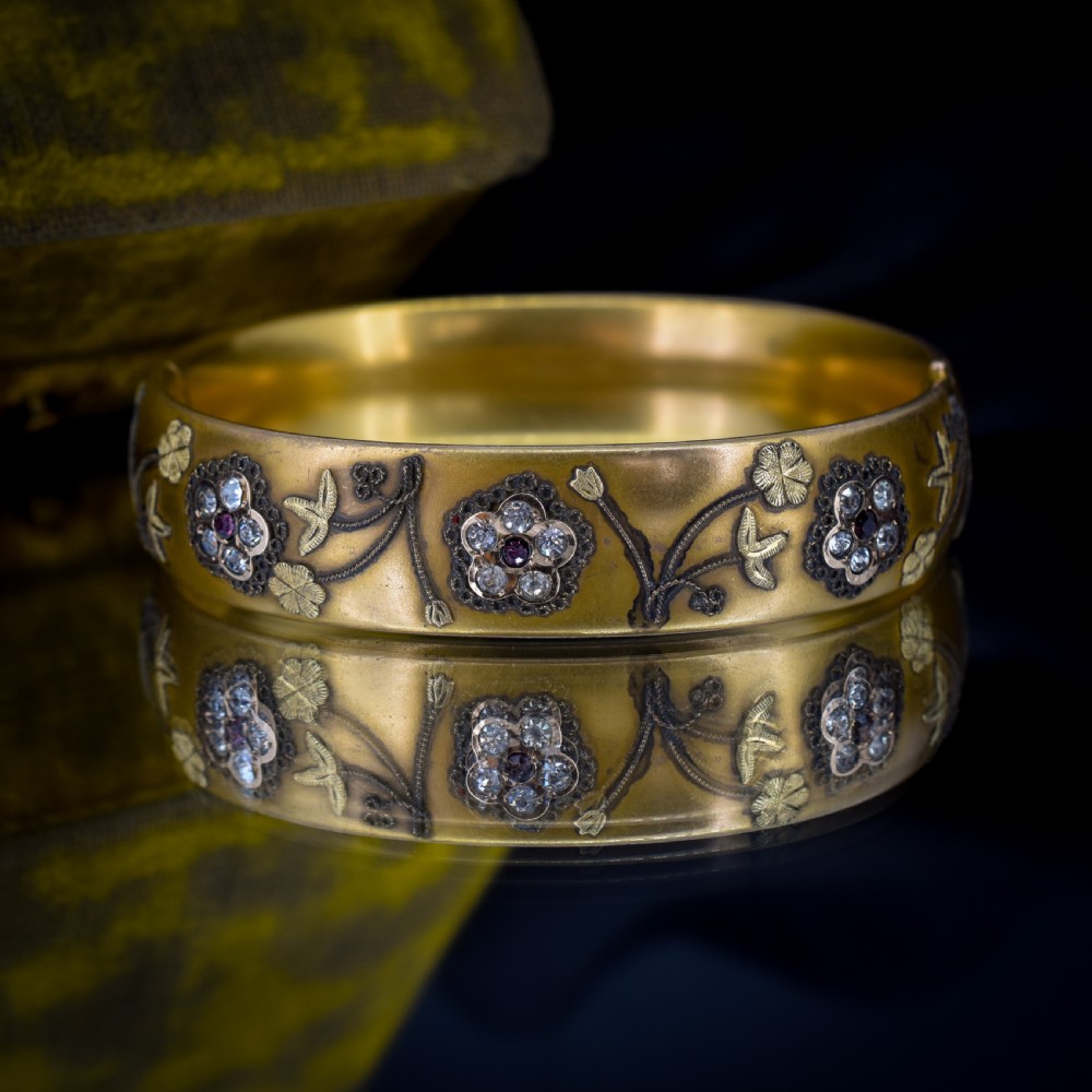 An antique gold-filled hinged bangle decorated with raised floral motifs with red and clear paste stone centres. View III