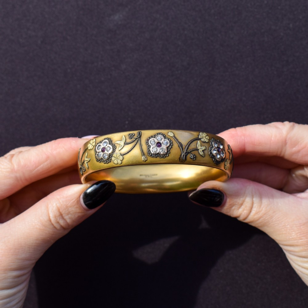 An antique gold-filled hinged bangle decorated with raised floral motifs with red and clear paste stone centres. View V