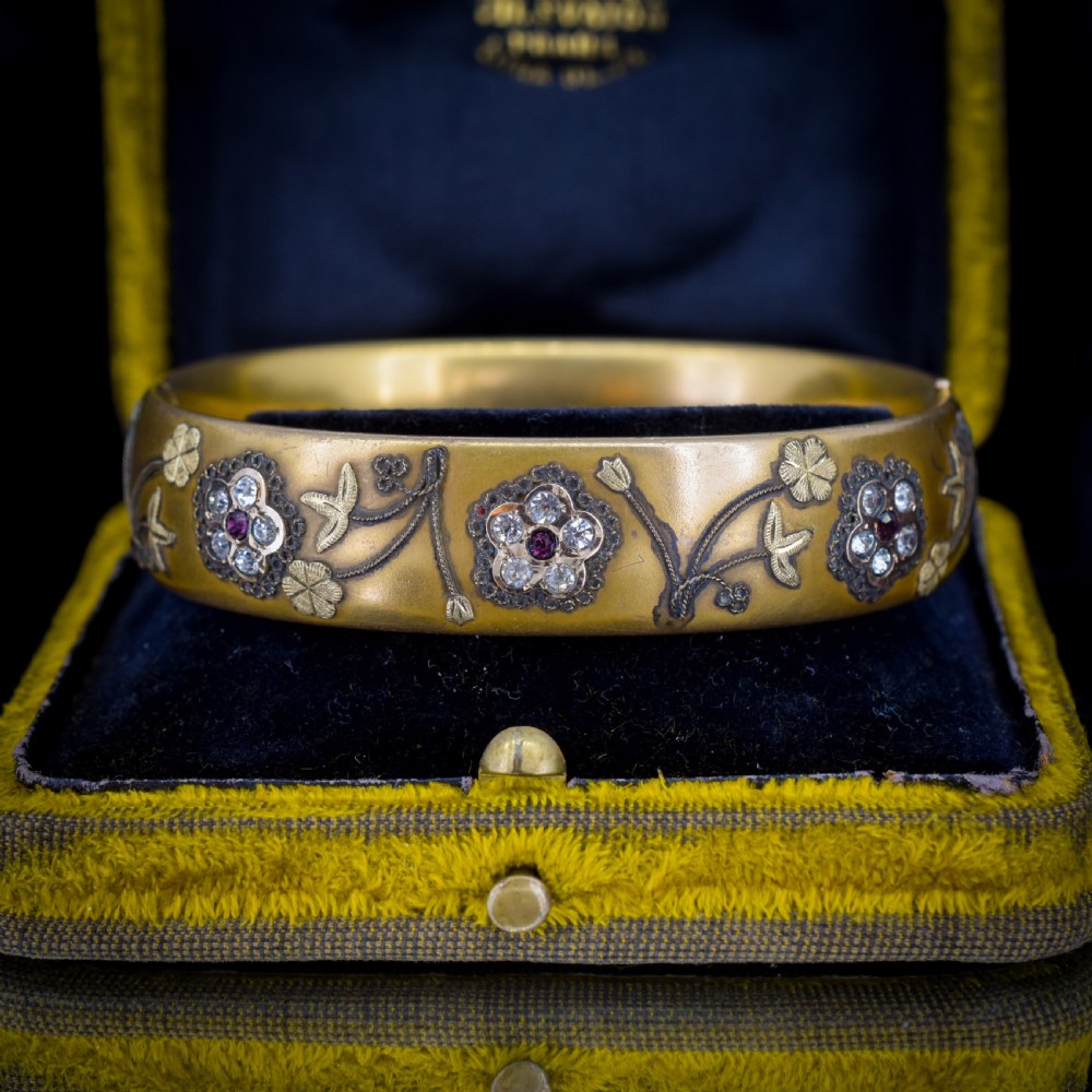 An antique gold-filled hinged bangle decorated with raised floral motifs with red and clear paste stone centres. View VI