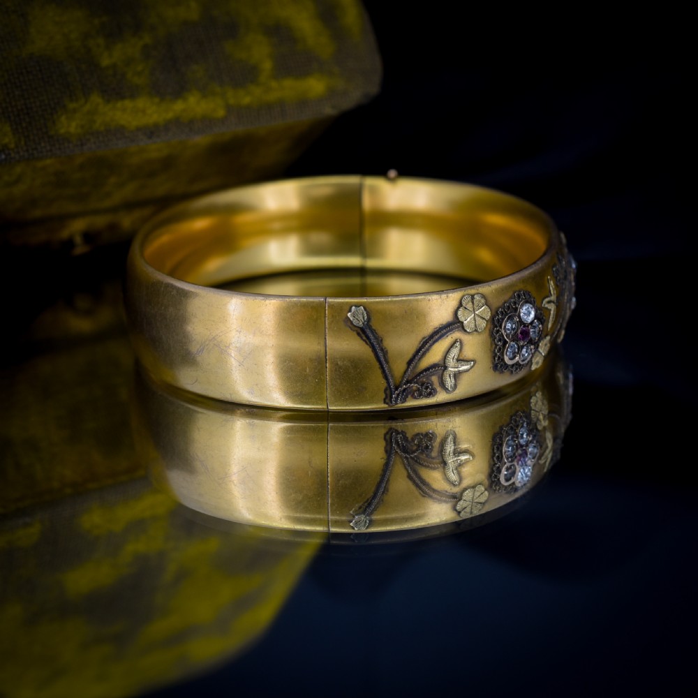 An antique gold-filled hinged bangle decorated with raised floral motifs with red and clear paste stone centres. View VII