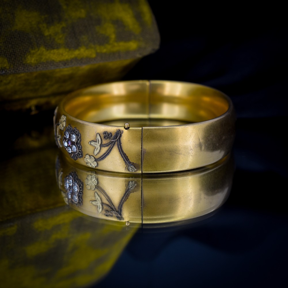 An antique gold-filled hinged bangle decorated with raised floral motifs with red and clear paste stone centres. View IX