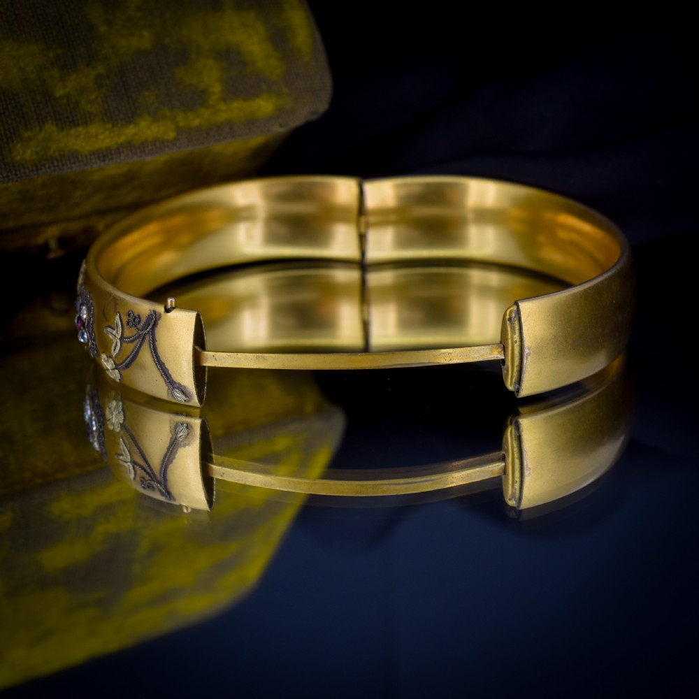 An antique gold-filled hinged bangle decorated with raised floral motifs with red and clear paste stone centres. View X
