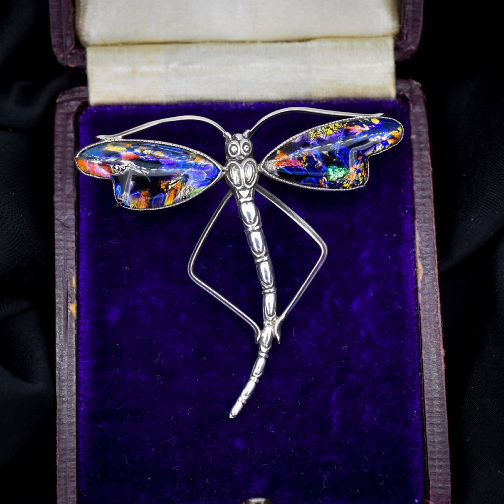 An Art Deco sterling silver dragonfly brooch featuring a stylized segmented body and iridescent blue and orange wing inserts.