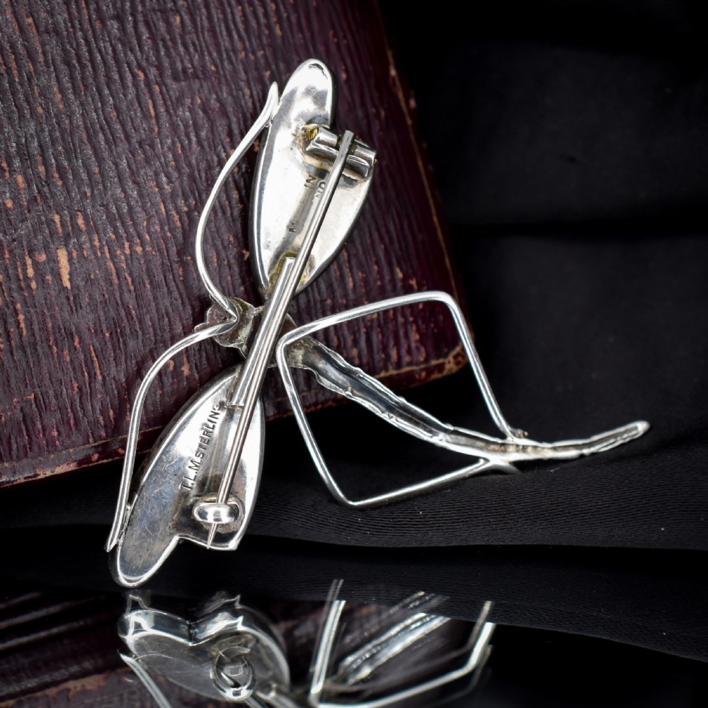 An Art Deco sterling silver dragonfly brooch featuring a stylized segmented body and iridescent blue and orange wing inserts. View VIII