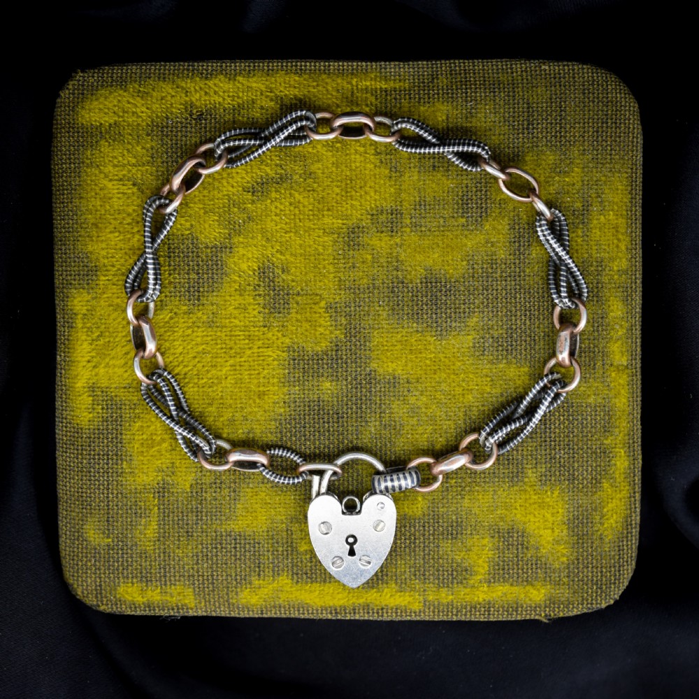 An antique silver and rose gold link bracelet featuring niello patterned twist links and a silver heart-shaped padlock clasp.