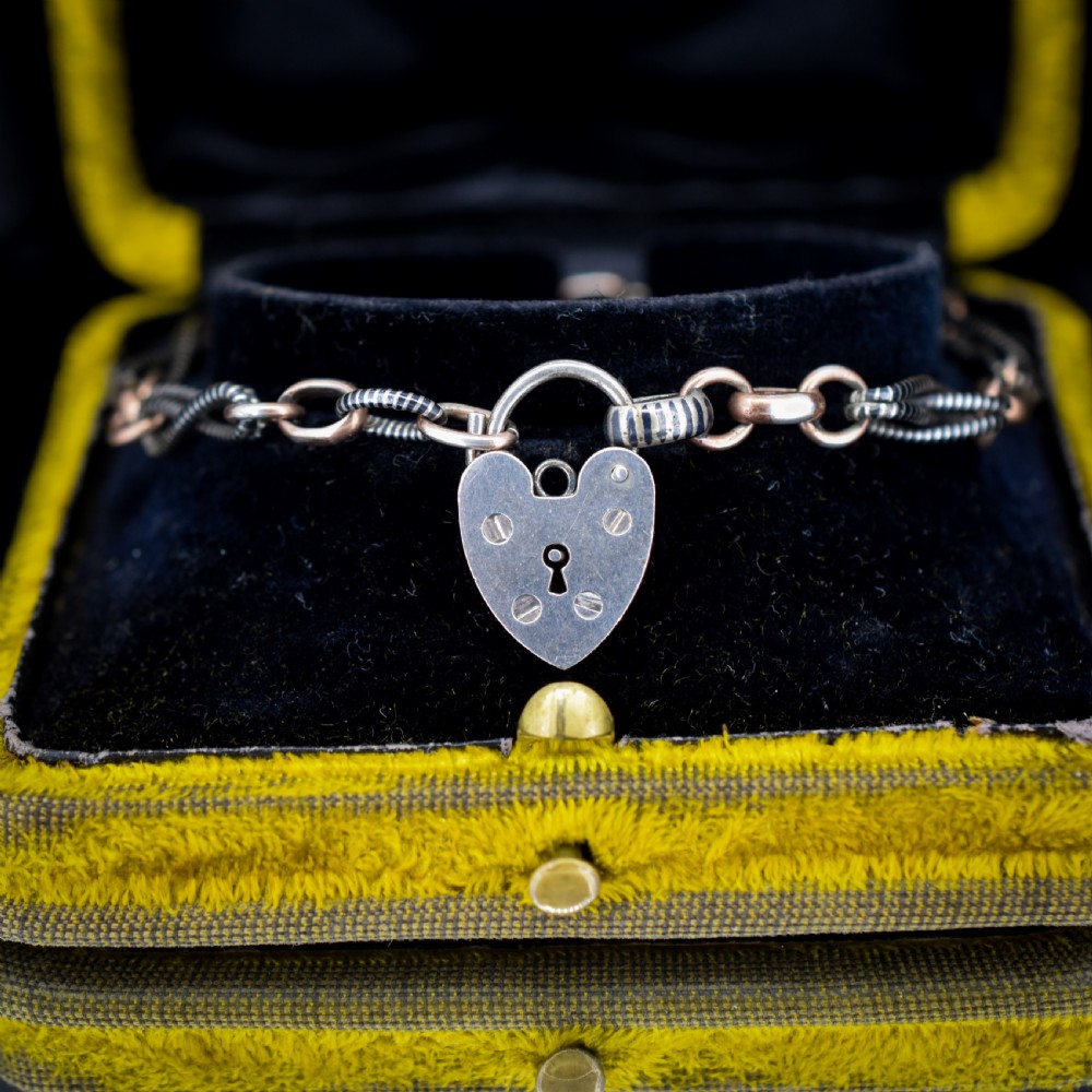 An antique silver and rose gold link bracelet featuring niello patterned twist links and a silver heart-shaped padlock clasp. View V