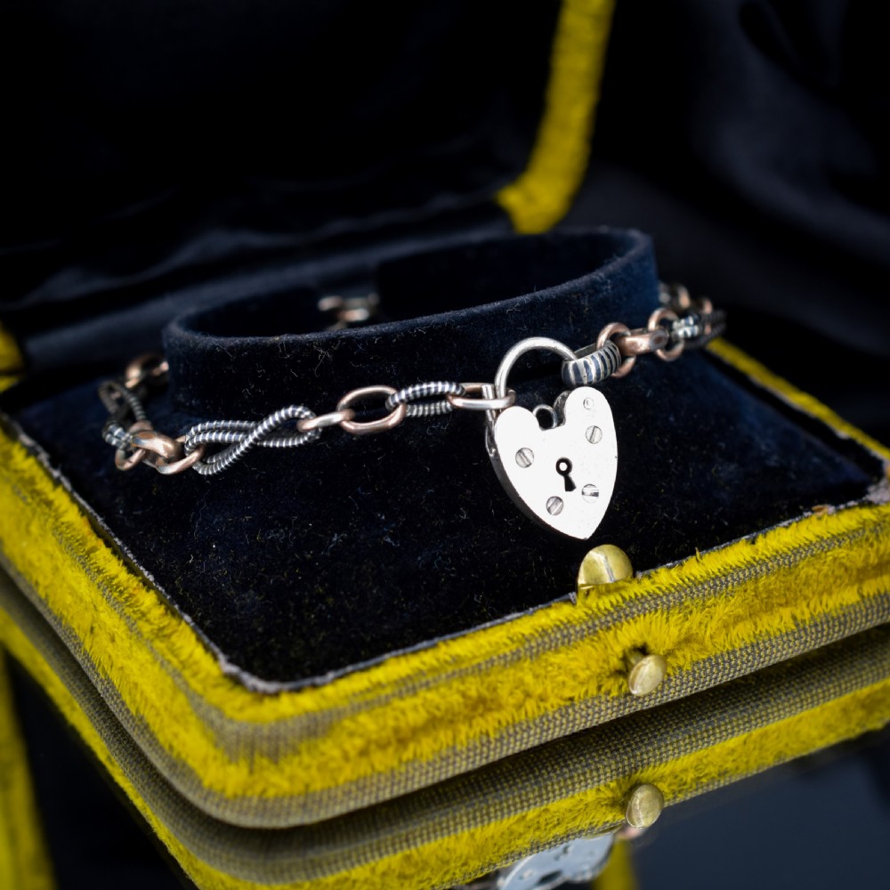 An antique silver and rose gold link bracelet featuring niello patterned twist links and a silver heart-shaped padlock clasp. View VI
