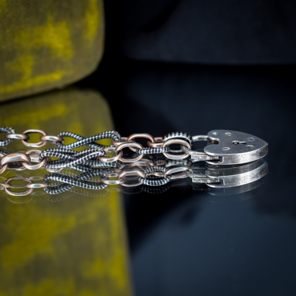 An antique silver and rose gold link bracelet featuring niello patterned twist links and a silver heart-shaped padlock clasp. View IX