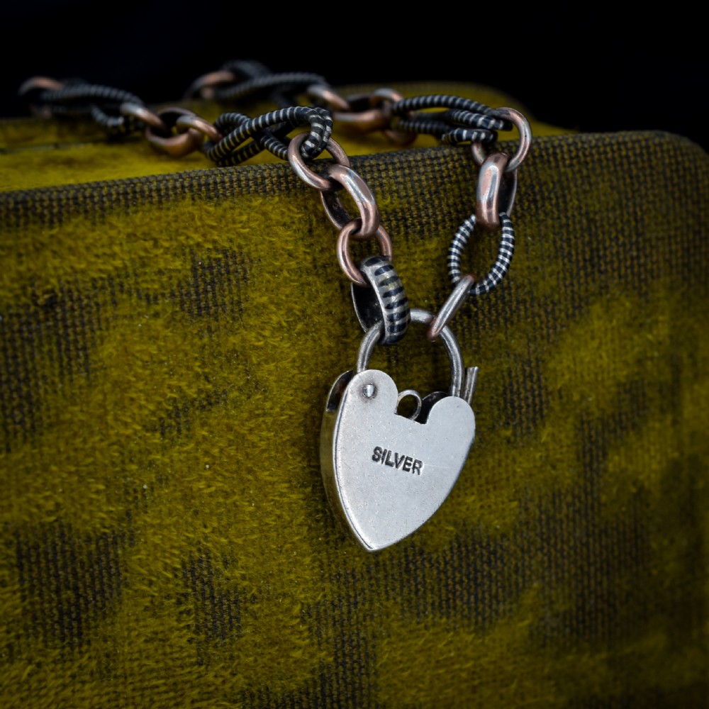 An antique silver and rose gold link bracelet featuring niello patterned twist links and a silver heart-shaped padlock clasp. View X