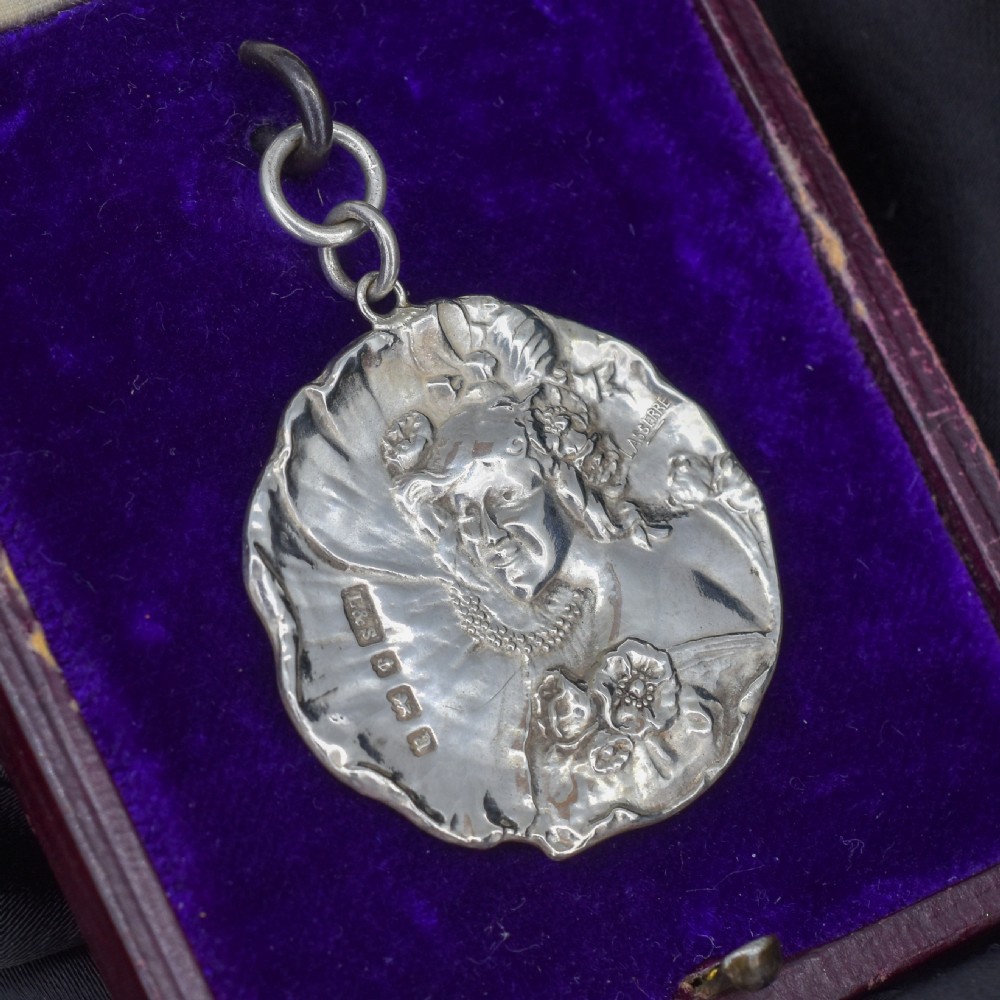 A circular Art Nouveau sterling silver pendant featuring a relief portrait of a woman surrounded by floral motifs and hallmarked on the front surface. View VI