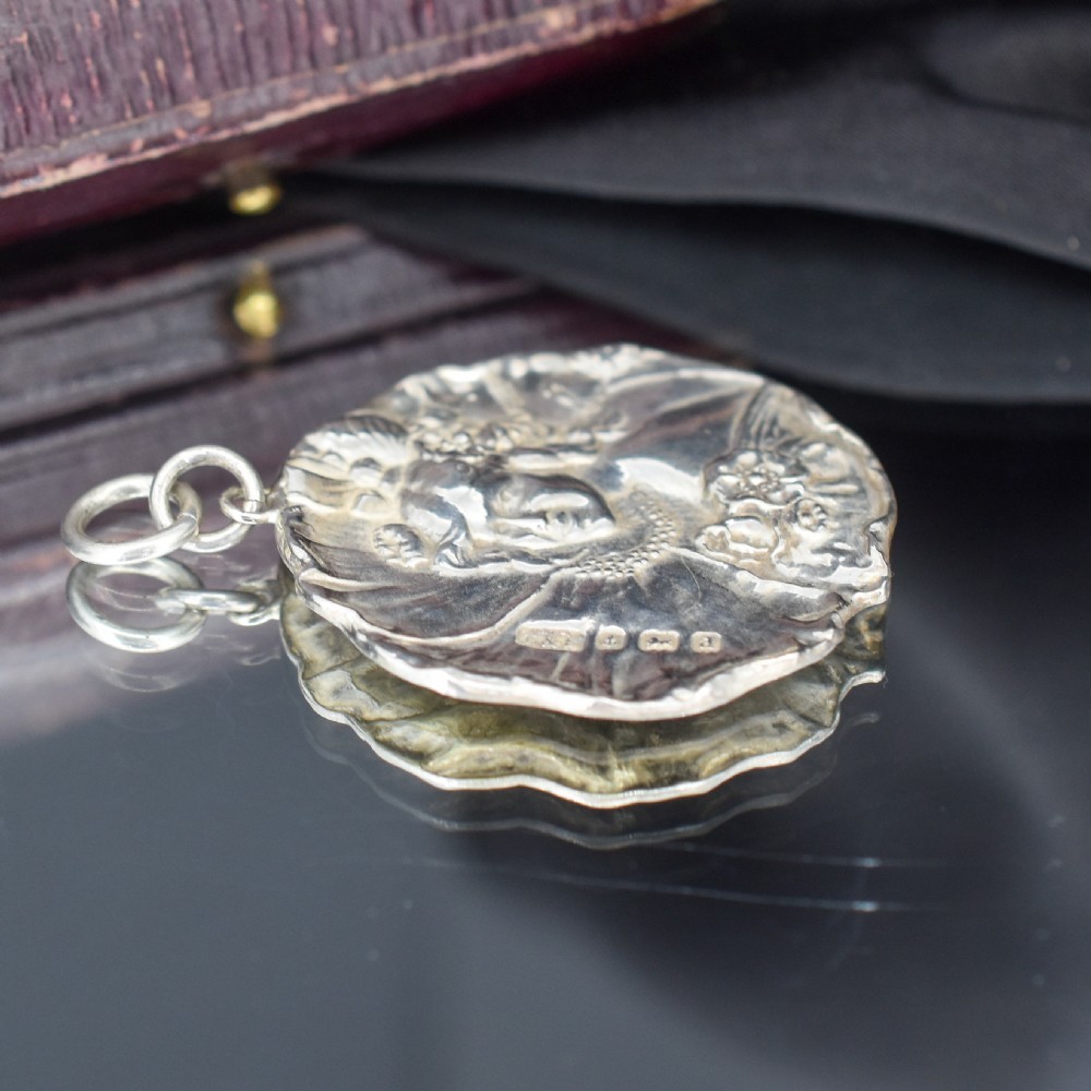 A circular Art Nouveau sterling silver pendant featuring a relief portrait of a woman surrounded by floral motifs and hallmarked on the front surface. View VII