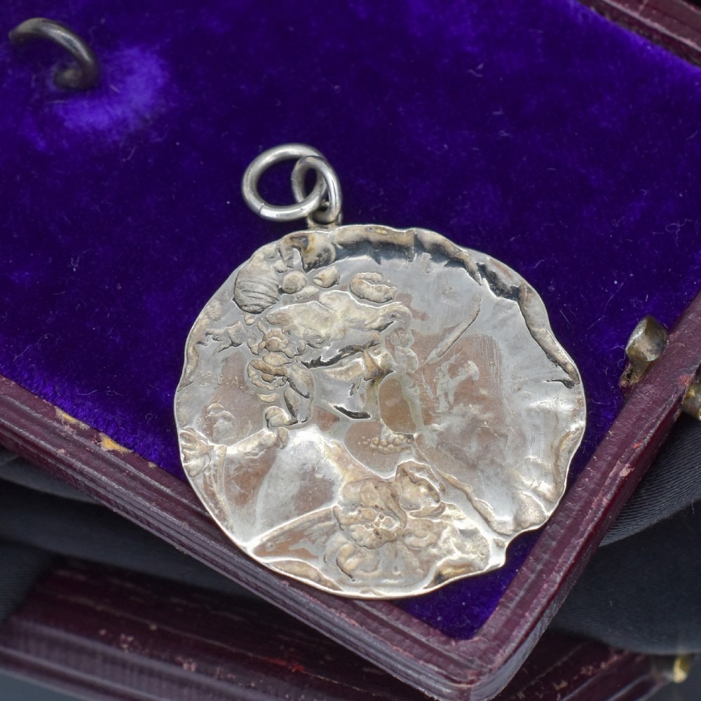 A circular Art Nouveau sterling silver pendant featuring a relief portrait of a woman surrounded by floral motifs and hallmarked on the front surface. View VIII
