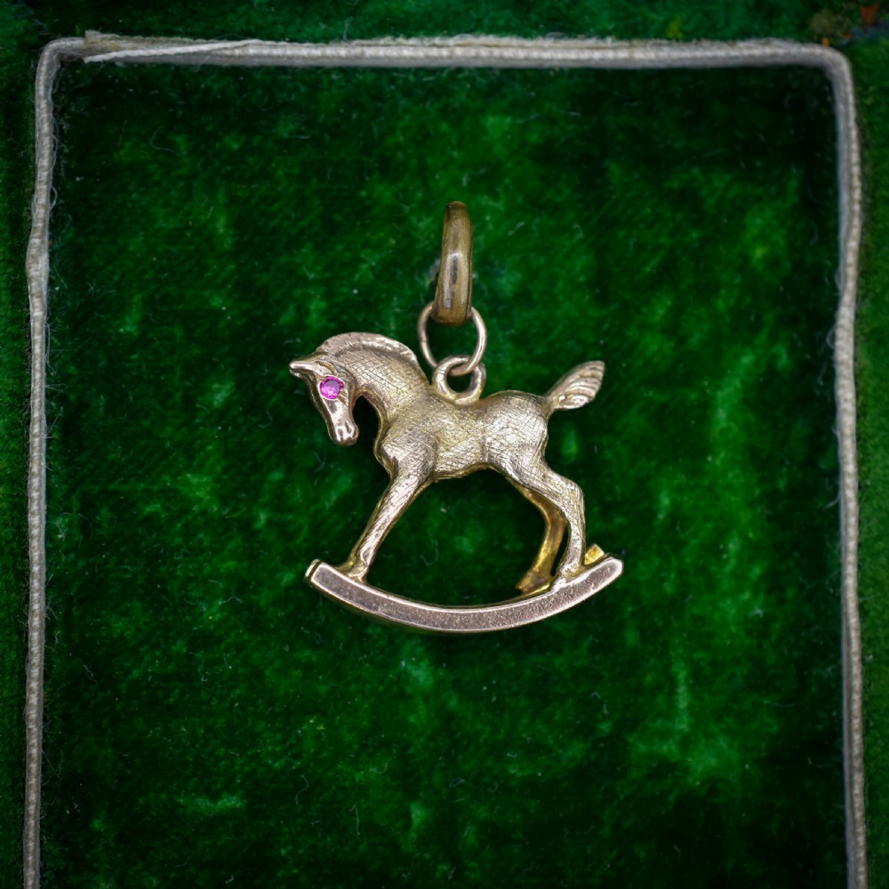 A 9ct yellow gold rocking horse charm featuring textured metalwork and a small pink gemstone eye.