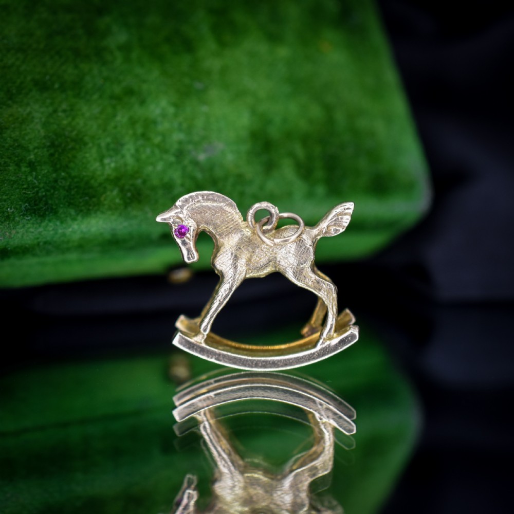 A 9ct yellow gold rocking horse charm featuring textured metalwork and a small pink gemstone eye. View V
