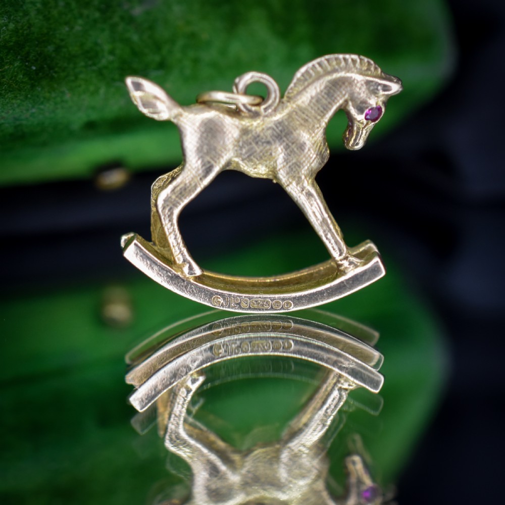 A 9ct yellow gold rocking horse charm featuring textured metalwork and a small pink gemstone eye. View VII