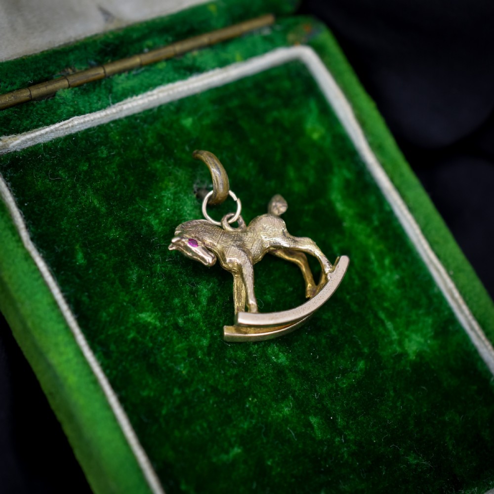 A 9ct yellow gold rocking horse charm featuring textured metalwork and a small pink gemstone eye. View X
