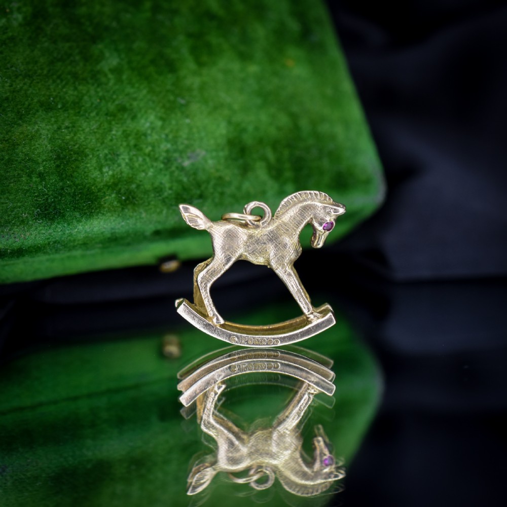 A 9ct yellow gold rocking horse charm featuring textured metalwork and a small pink gemstone eye. View XII