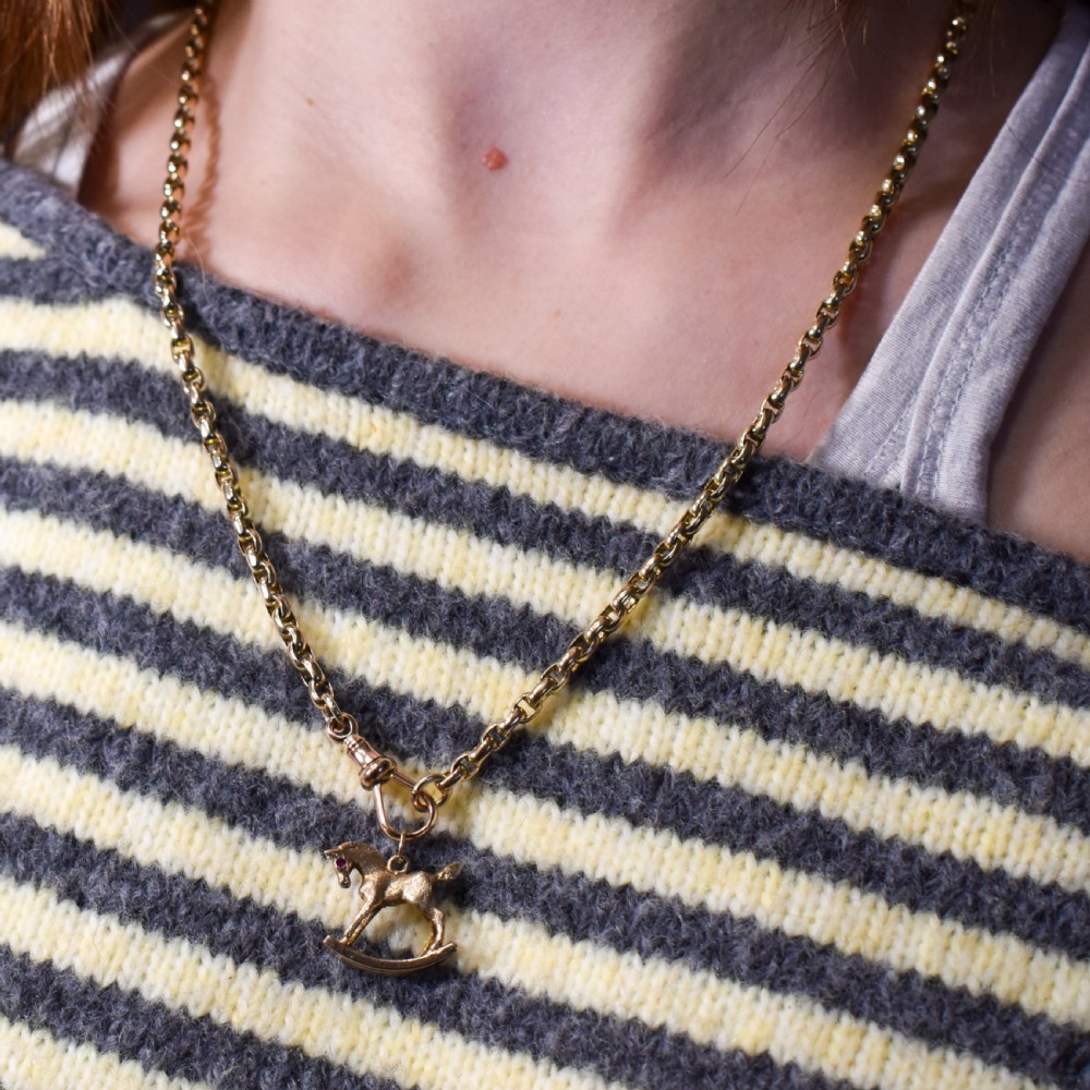 A 9ct yellow gold rocking horse charm featuring textured metalwork and a small pink gemstone eye. View XIV