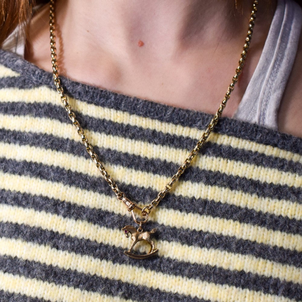 A 9ct yellow gold rocking horse charm featuring textured metalwork and a small pink gemstone eye. View XV