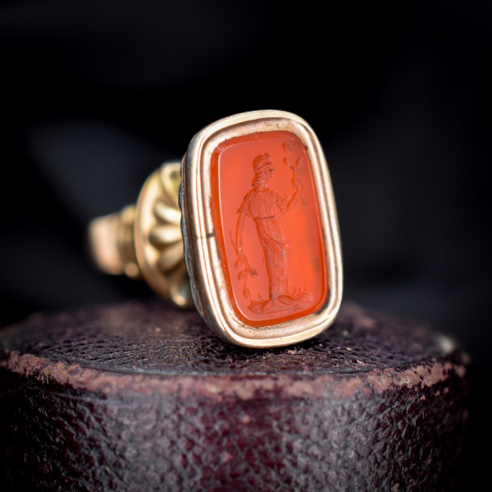An antique gold fob pendant set with a rectangular orange carnelian gemstone carved with a classical standing figure holding a branch.